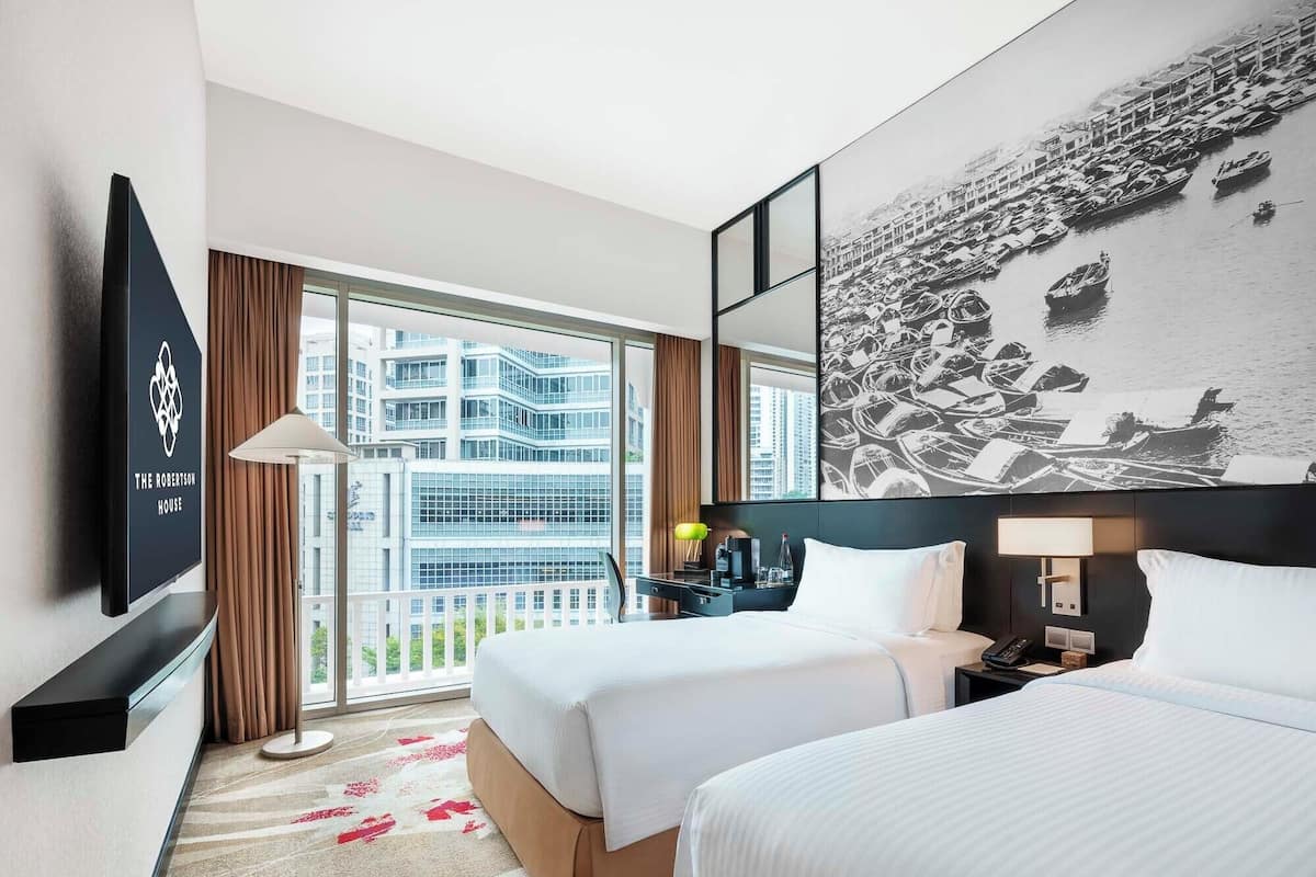 Habitación de hotel con dos camas, televisión, escritorio, lámpara y una ventana grande con vistas a la ciudad.