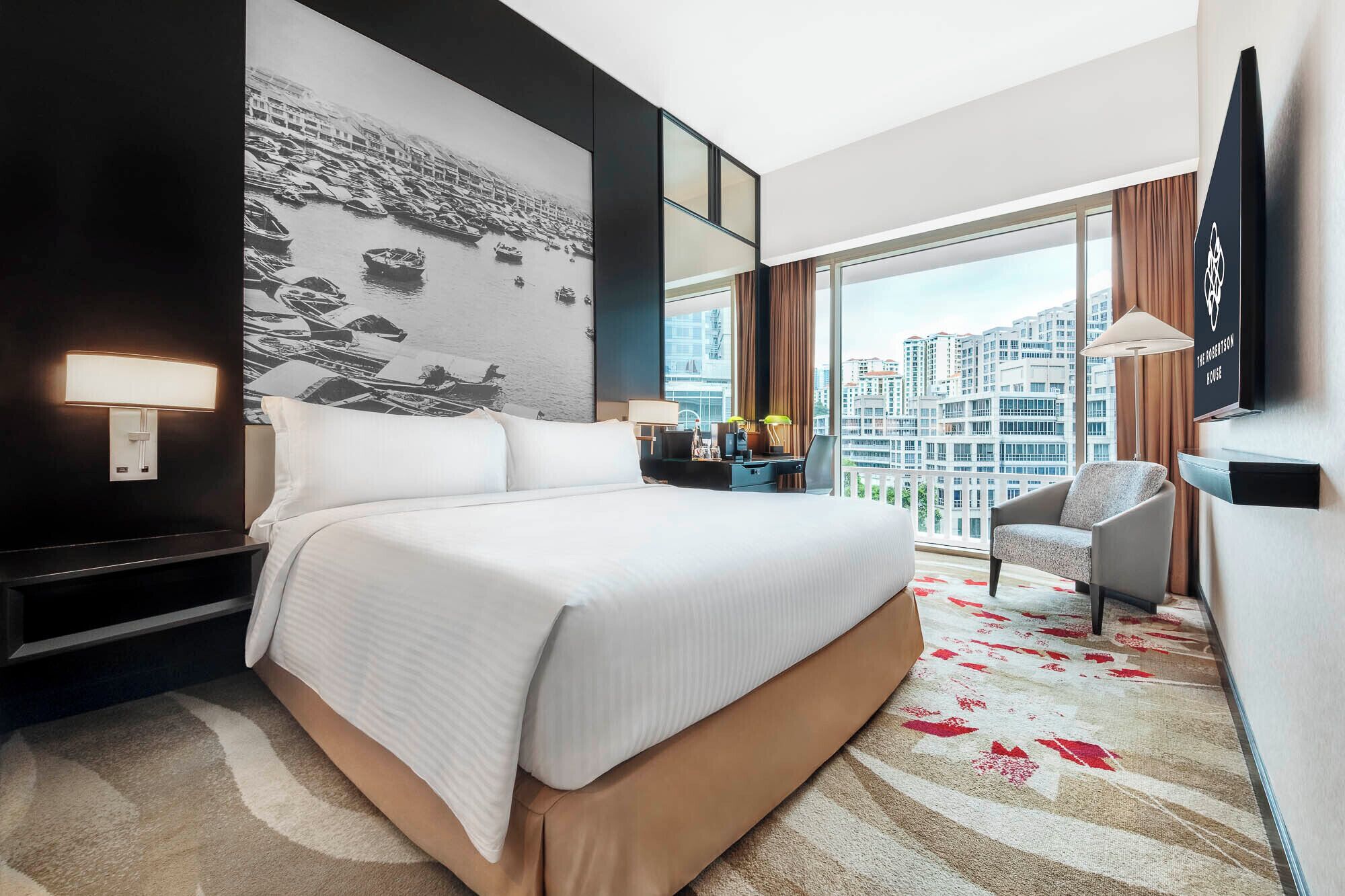 Habitación de hotel con una cama grande, un escritorio, una silla, un televisor y vistas a la ciudad.