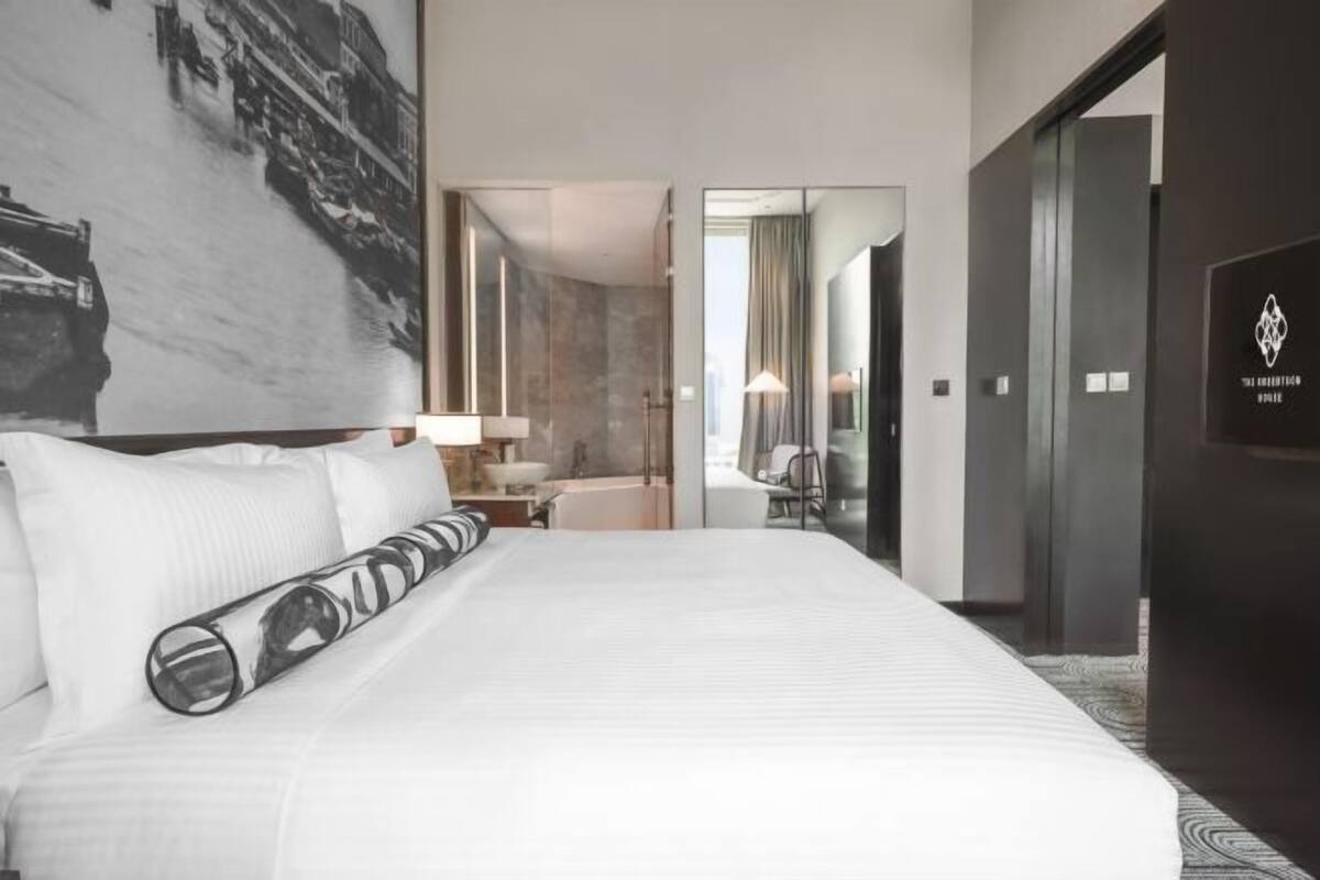 A hotel room with a large bed, a bathroom with a shower, and a view of a cityscape.