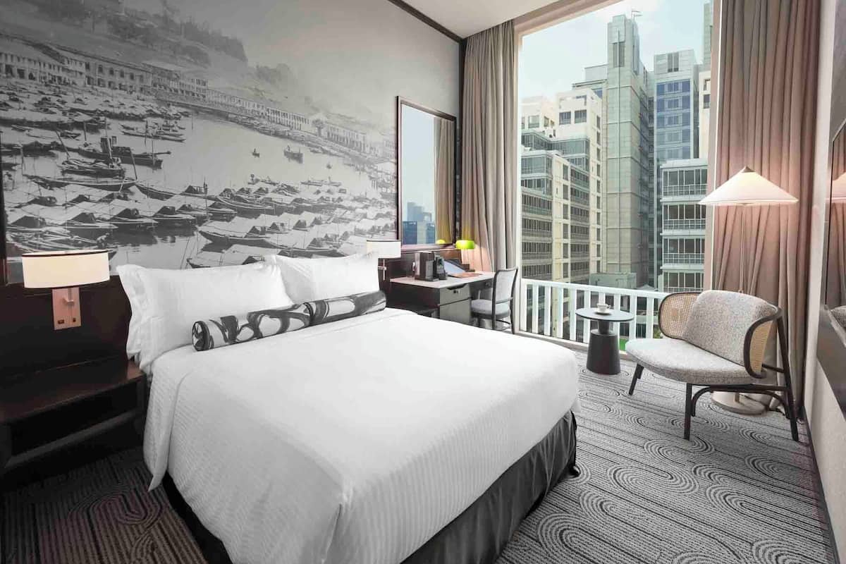 Habitación de hotel con una cama grande, un escritorio, una silla, un balcón con vistas a edificios y un mural en la pared.