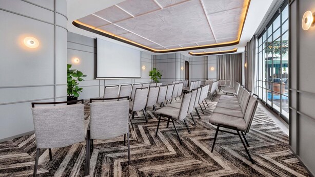 A conference room with a large screen, rows of chairs, and a patterned carpet. - Novotel Singapore Robertson Quay (Singapore)