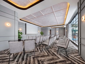 A conference room with a large screen, rows of chairs, and a patterned carpet.