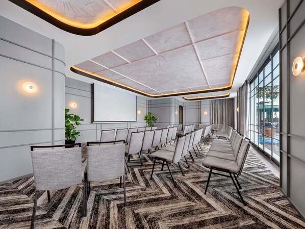 Un salón de conferencias con una pantalla grande, filas de sillas y una alfombra estampada.