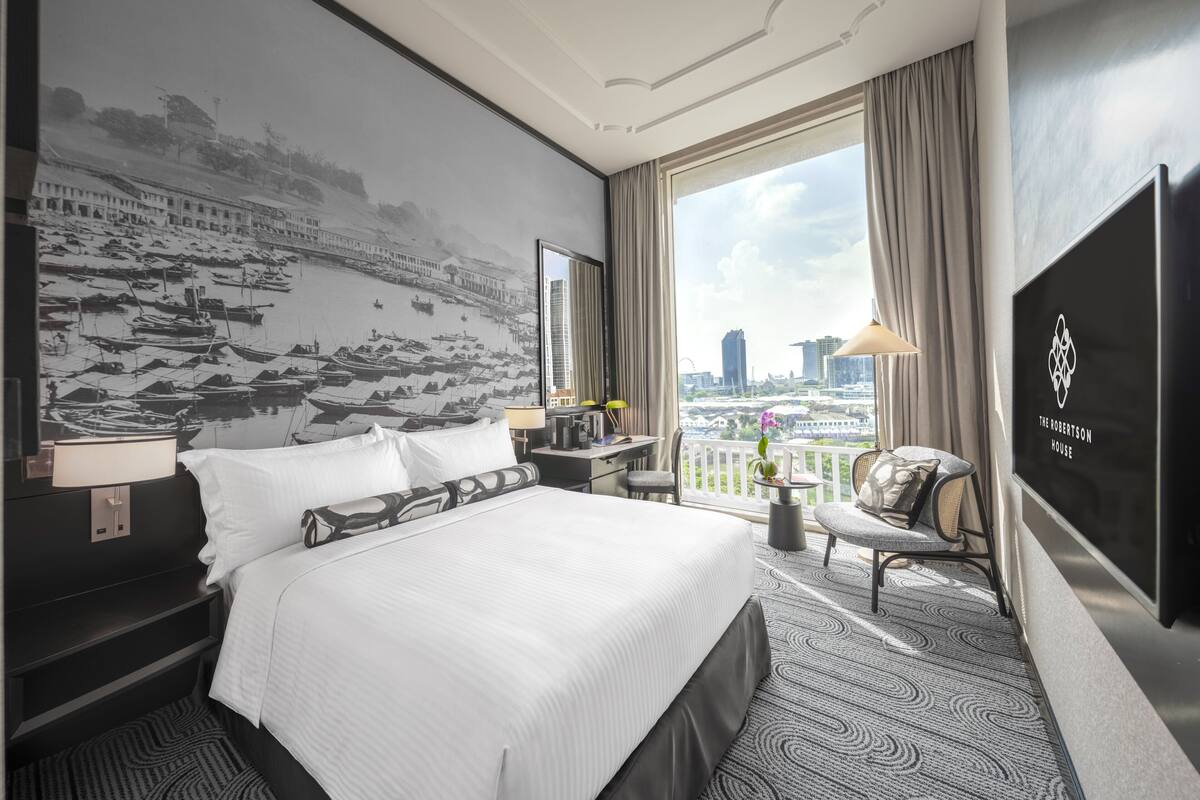 A hotel room with a large bed, a desk with a lamp, a chair, a television, and a view of the cityscape.