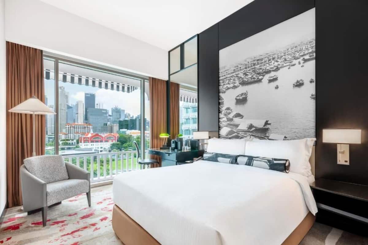 Habitación de hotel con una cama grande, una silla, un escritorio, vista a la ciudad y una obra de arte de gran tamaño en la pared.