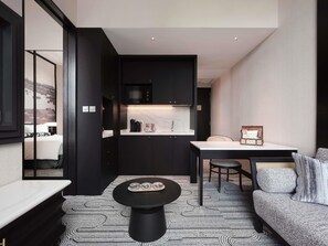 Una habitación de hotel moderna con kitchenette, un comedor con mesa y sillas, un sofá y una alfombra estampada.