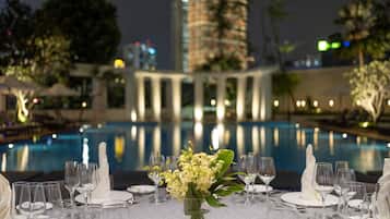 A formal dining table set for a meal with a view of a pool and a building in the background.