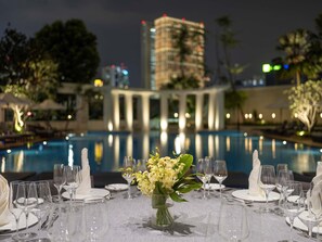 Mesa formal lista para una comida, con vista a una piscina y un edificio al fondo.