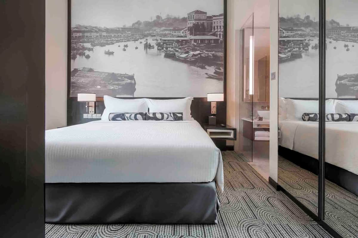 Habitación de hotel con una cama grande, una mesita de noche, un espejo y un cuadro colgado en la pared que muestra una vista acuática.