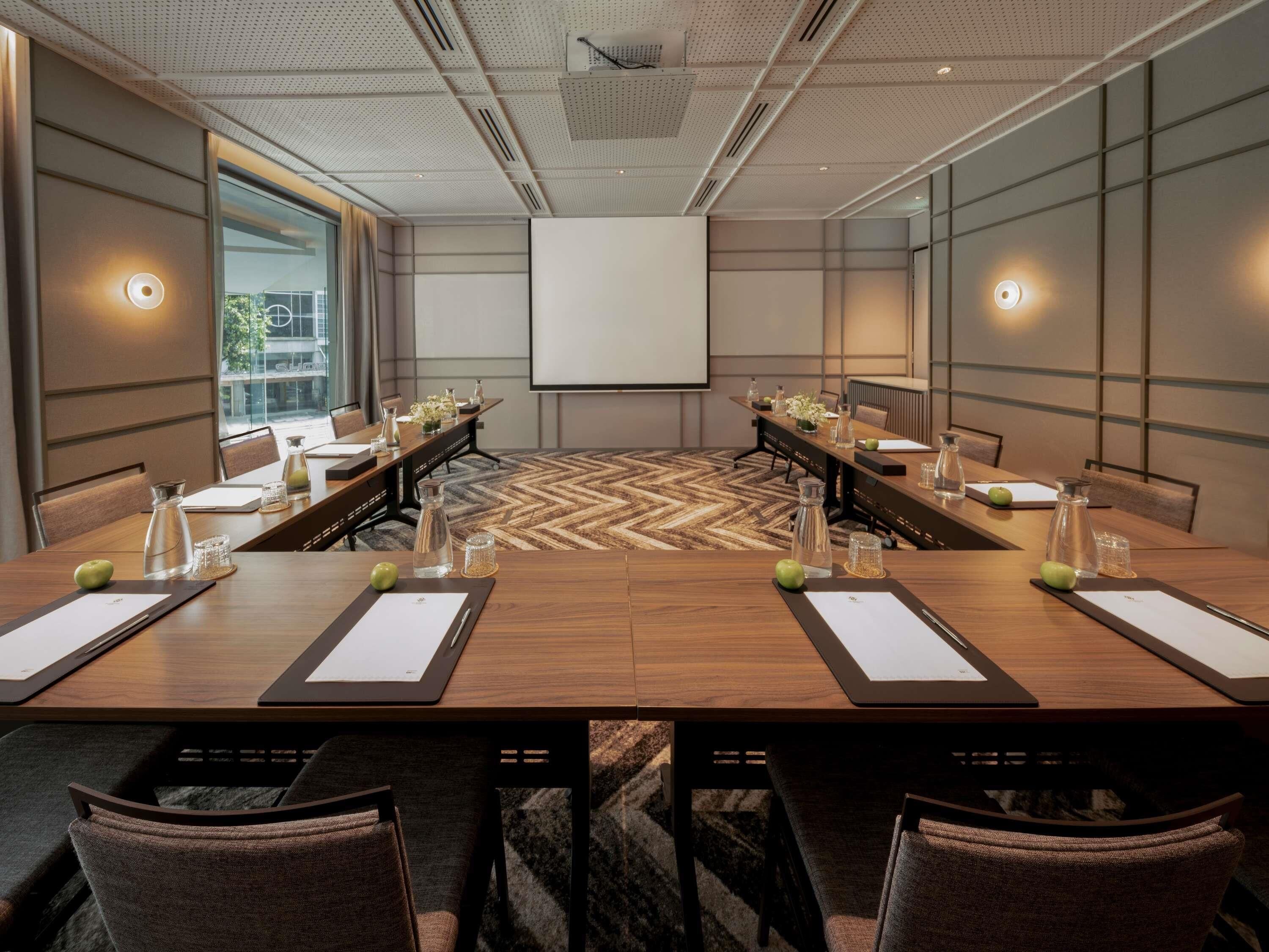 A conference room with a large table, chairs, a projector screen, and a view of the outdoors.