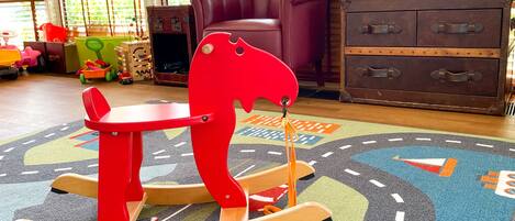 A room with a rocking horse, a purple sofa, and a wooden chest of drawers.