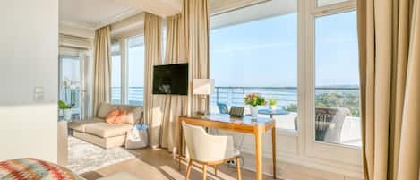 A modern hotel room with a balcony, a sofa, a desk, and a TV.