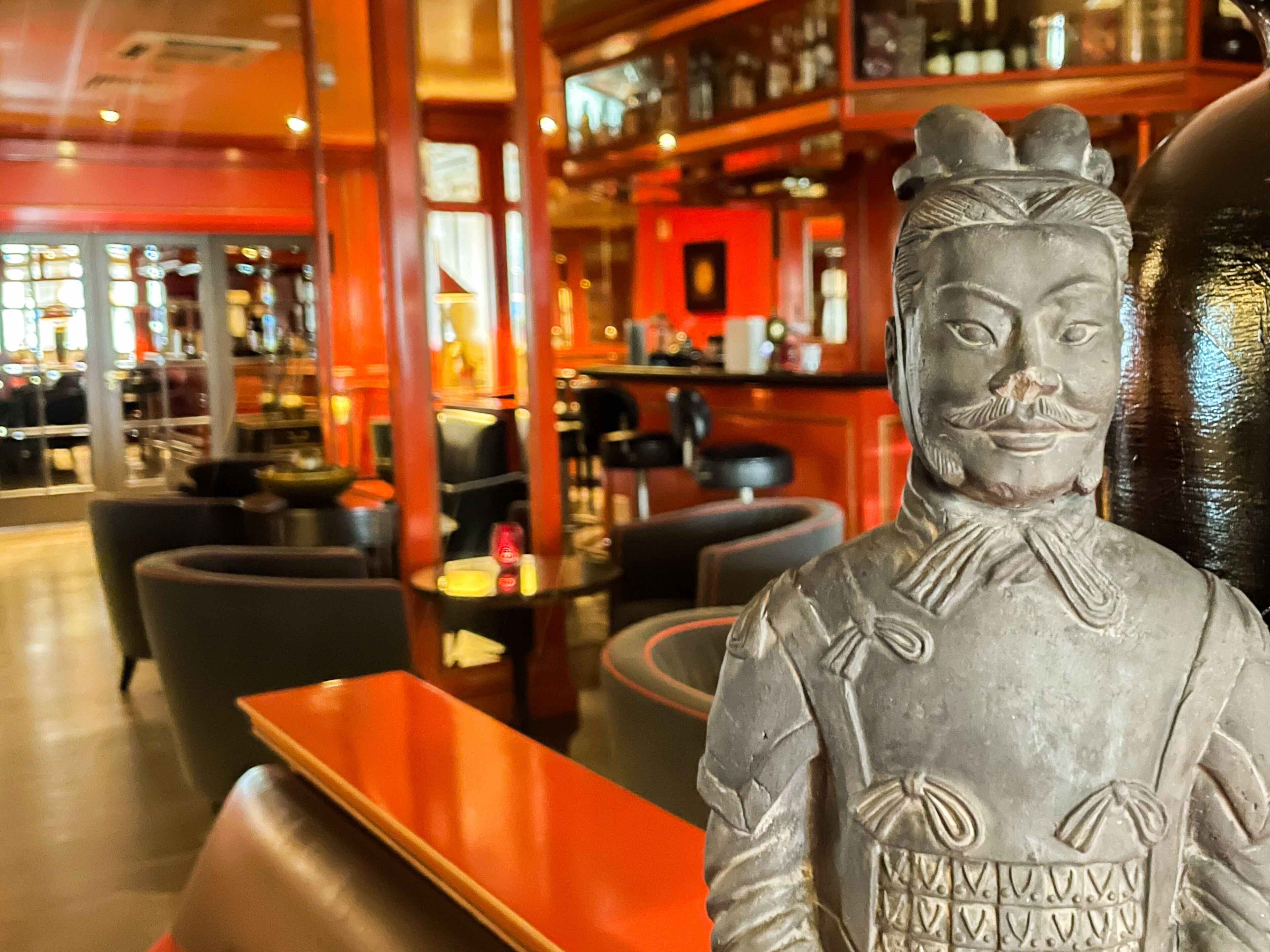 Una zona de bar con una estatua, asientos y estanterías llenas de botellas.