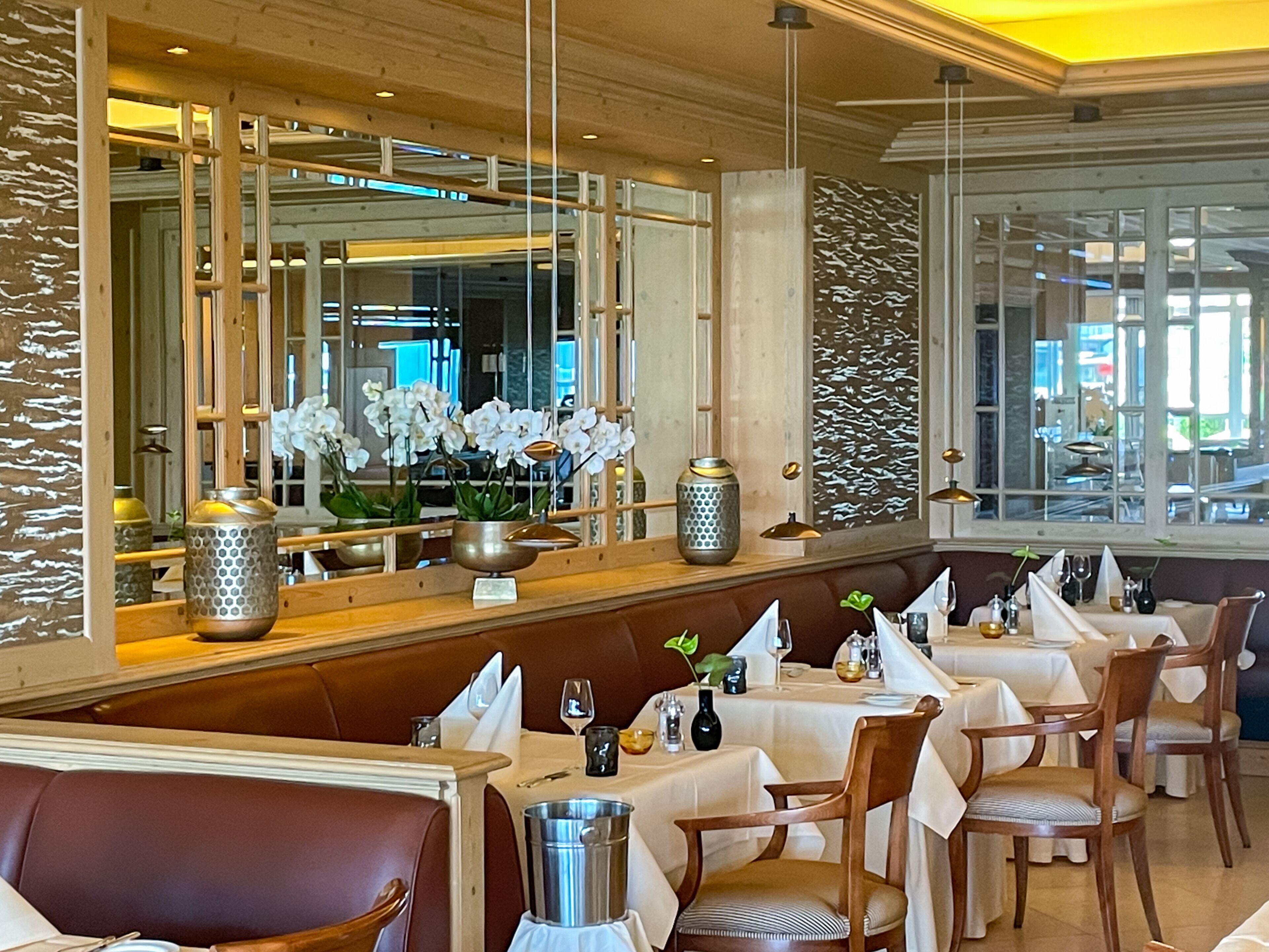 A restaurant with wooden paneling, white tablecloths, and a variety of table settings including wine glasses and cutlery.