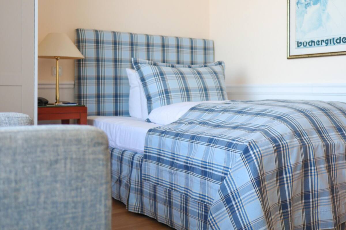 A neatly made bed with a plaid bedspread, a bedside lamp, and a framed picture on the wall.