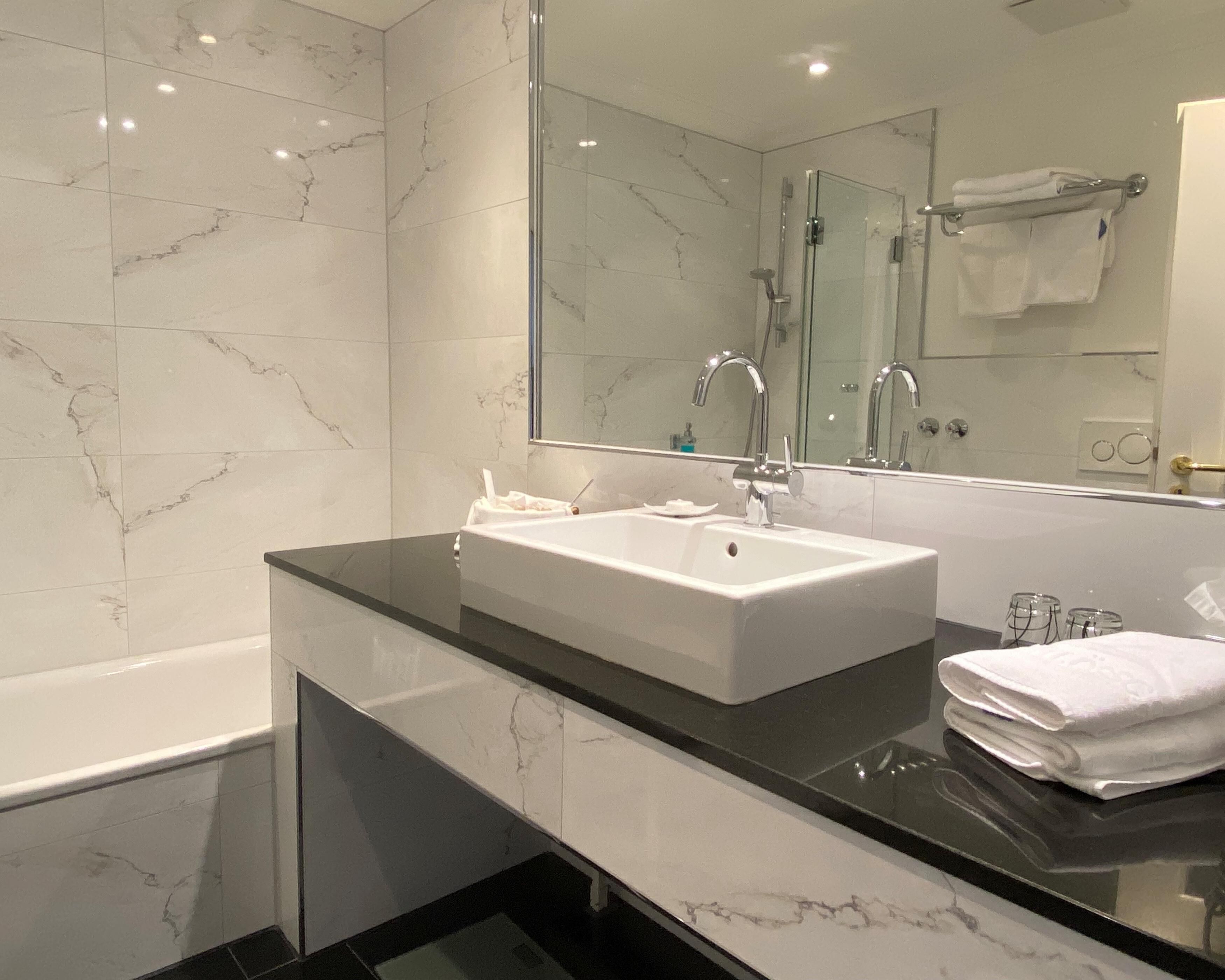 A modern bathroom with a white marble sink, black countertop, and a large mirror.