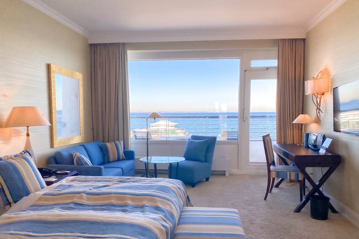 A hotel room with a bed, two sofas, a desk, and a view of the sea.