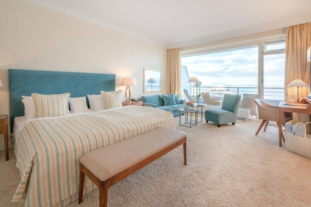 A hotel room with a large bed, a sofa, a desk, and a view of the sea.