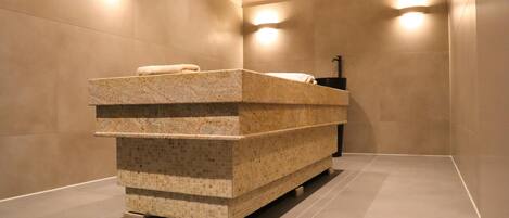 A modern bathroom with a freestanding granite sink, tiled walls, and built-in lighting.