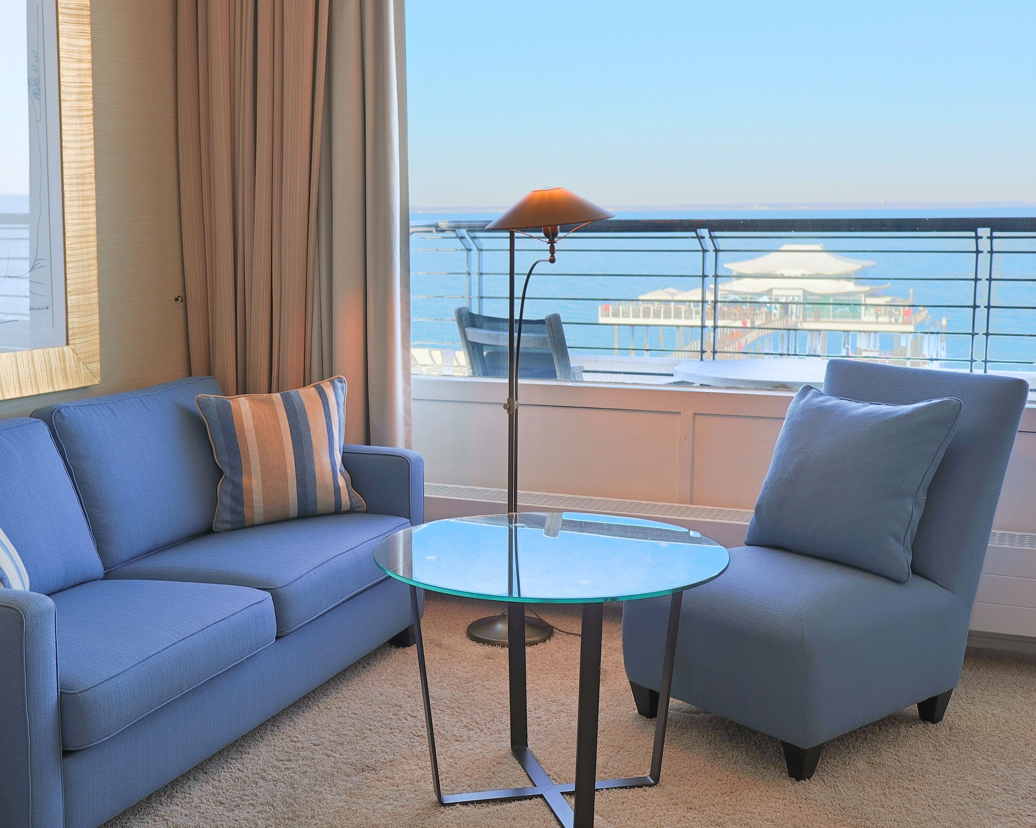 Un balcon avec une table en verre et deux chaises, un canapé et une lampe.
