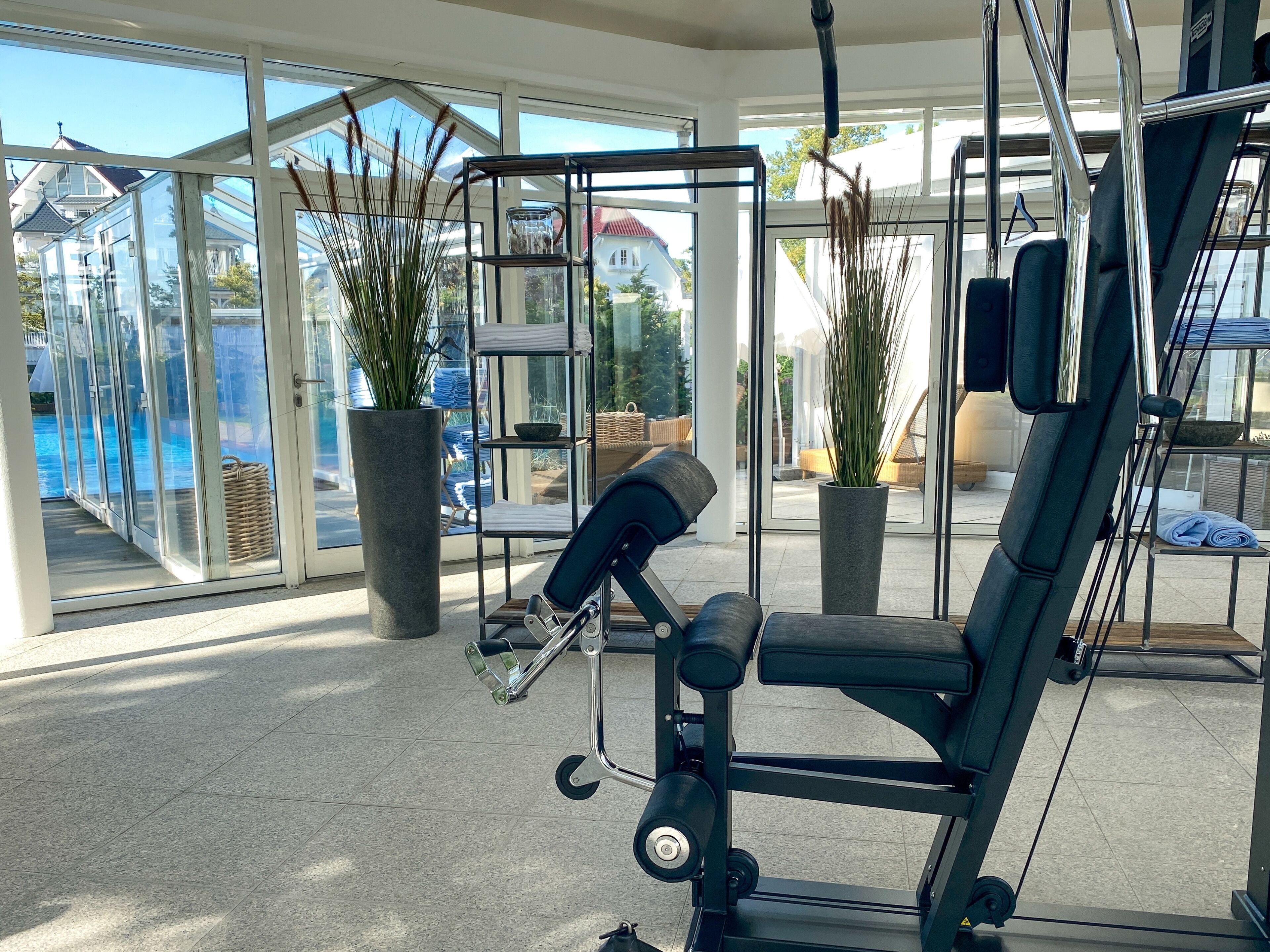 Et fitnesscenter med træningsudstyr, store vinduer og krukkeplanter.