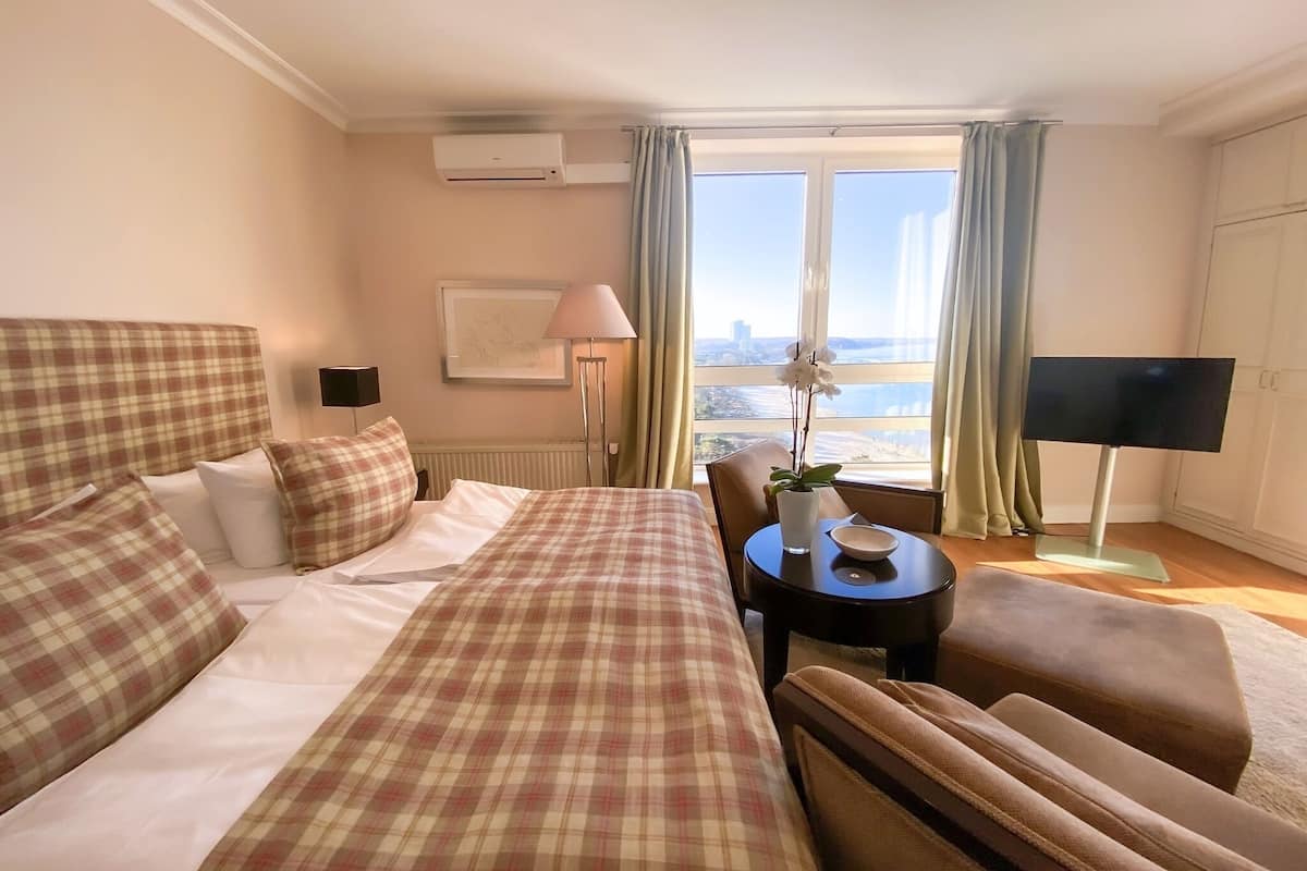 A hotel room with a large bed, a desk, a chair, a TV, and a window with a view of the city.