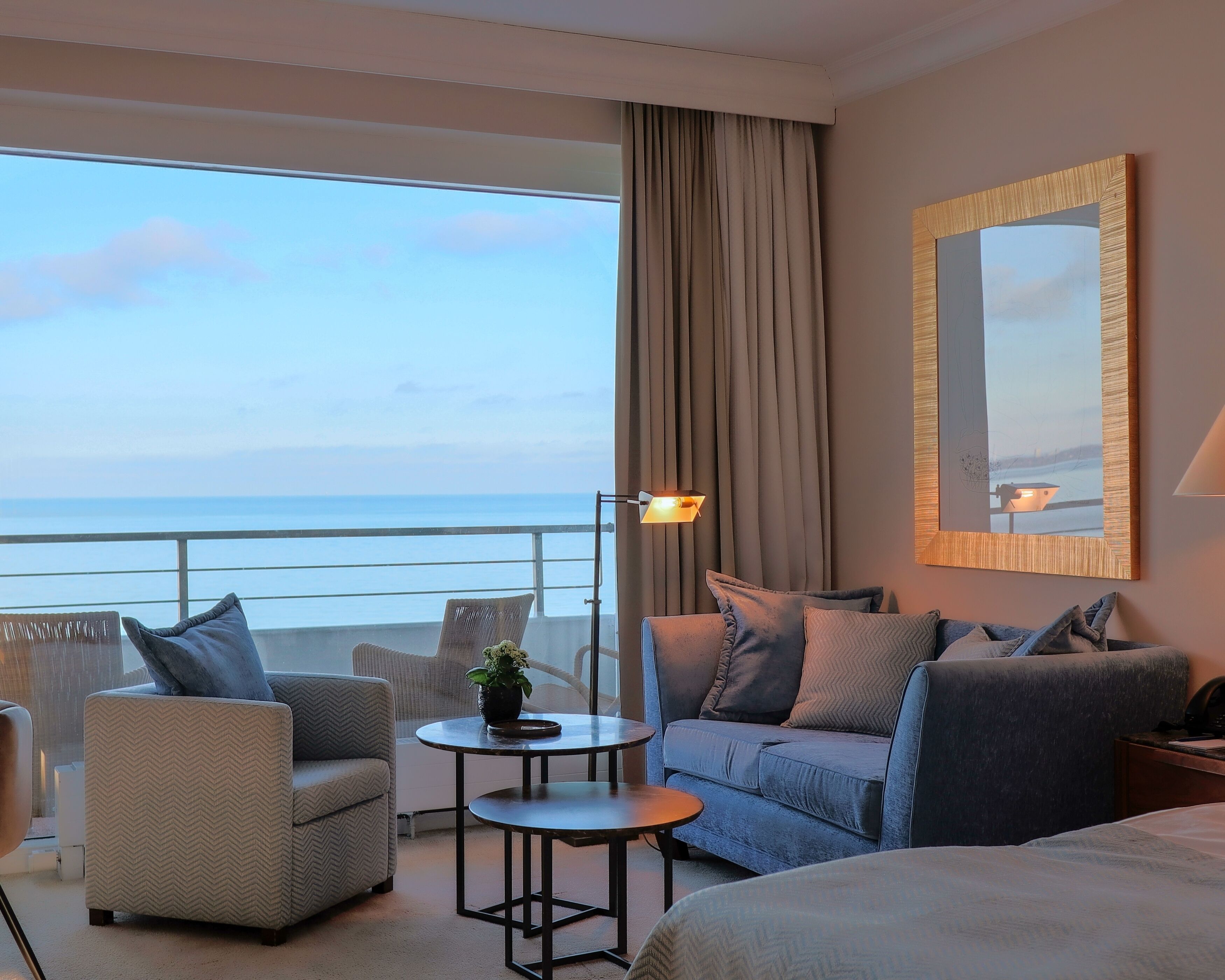 Una camera d'albergo con una grande finestra vista mare, un divano, un tavolino e una lampada.