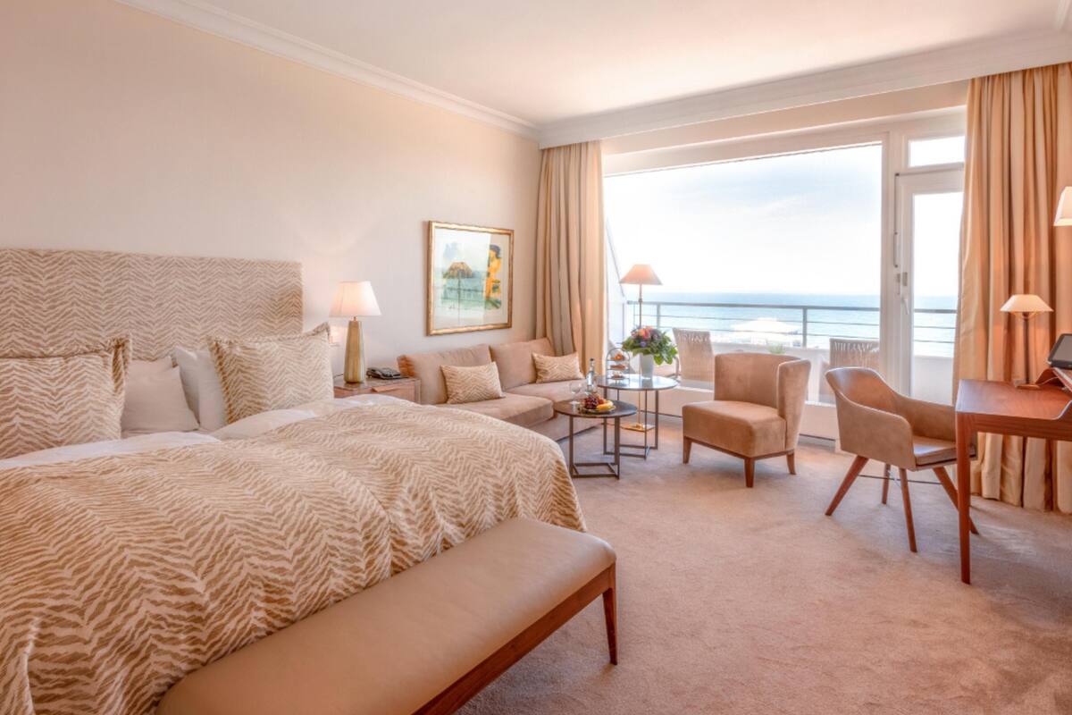 A hotel room with a large bed, a sofa, a desk, and a view of the ocean.