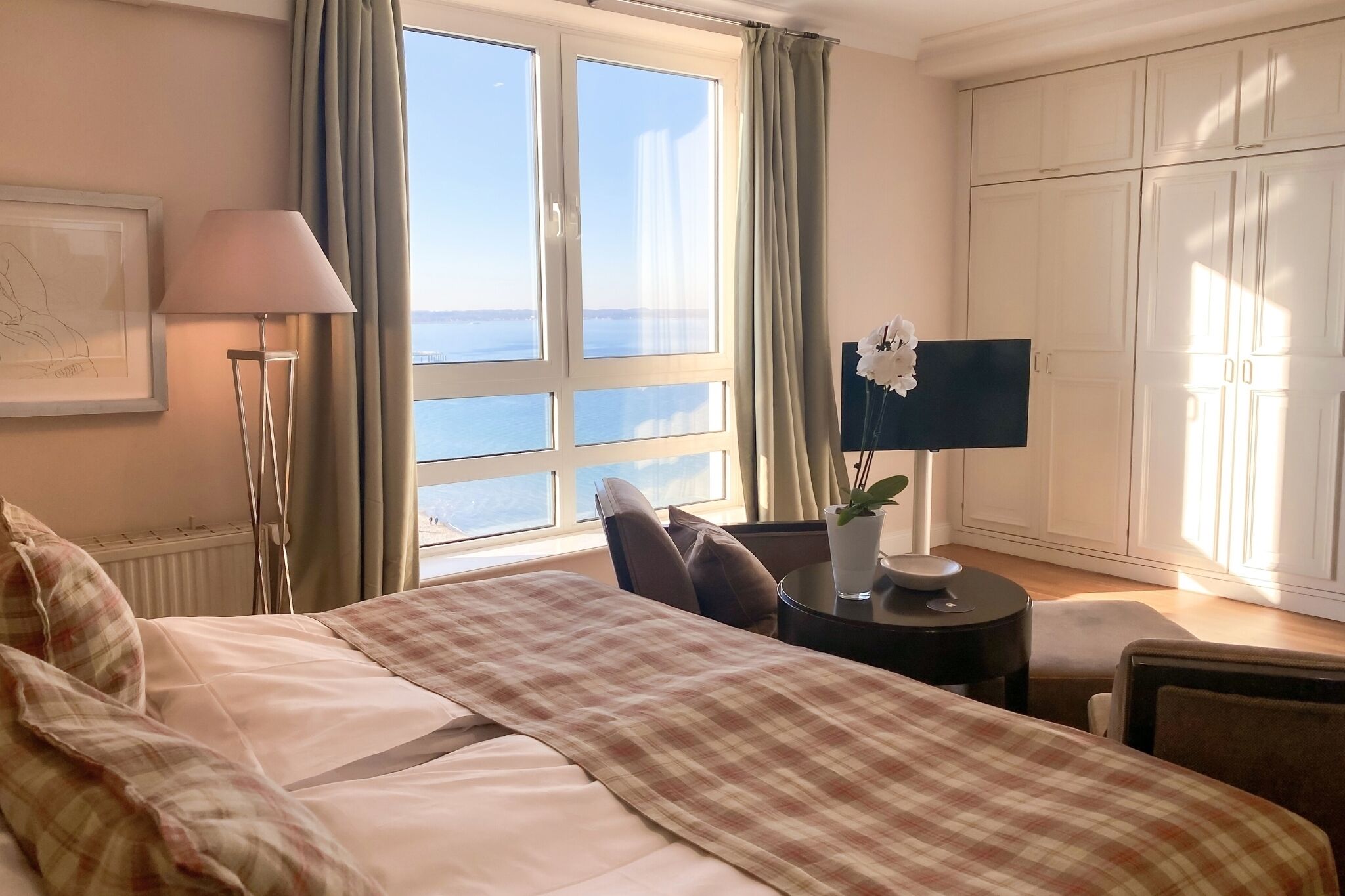 Une chambre d’hôtel avec un grand lit, un bureau avec une lampe, une vue sur la mer et une armoire.