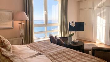 Une chambre d’hôtel avec un grand lit, un bureau avec une lampe, une vue sur la mer et une armoire.
