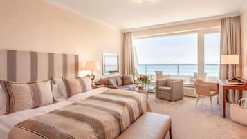 A hotel room with a large bed, a desk, a chair, and a view of the sea.
