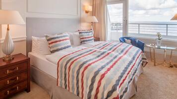 A hotel room with a large bed, two bedside lamps, a small table, and a view of the sea.