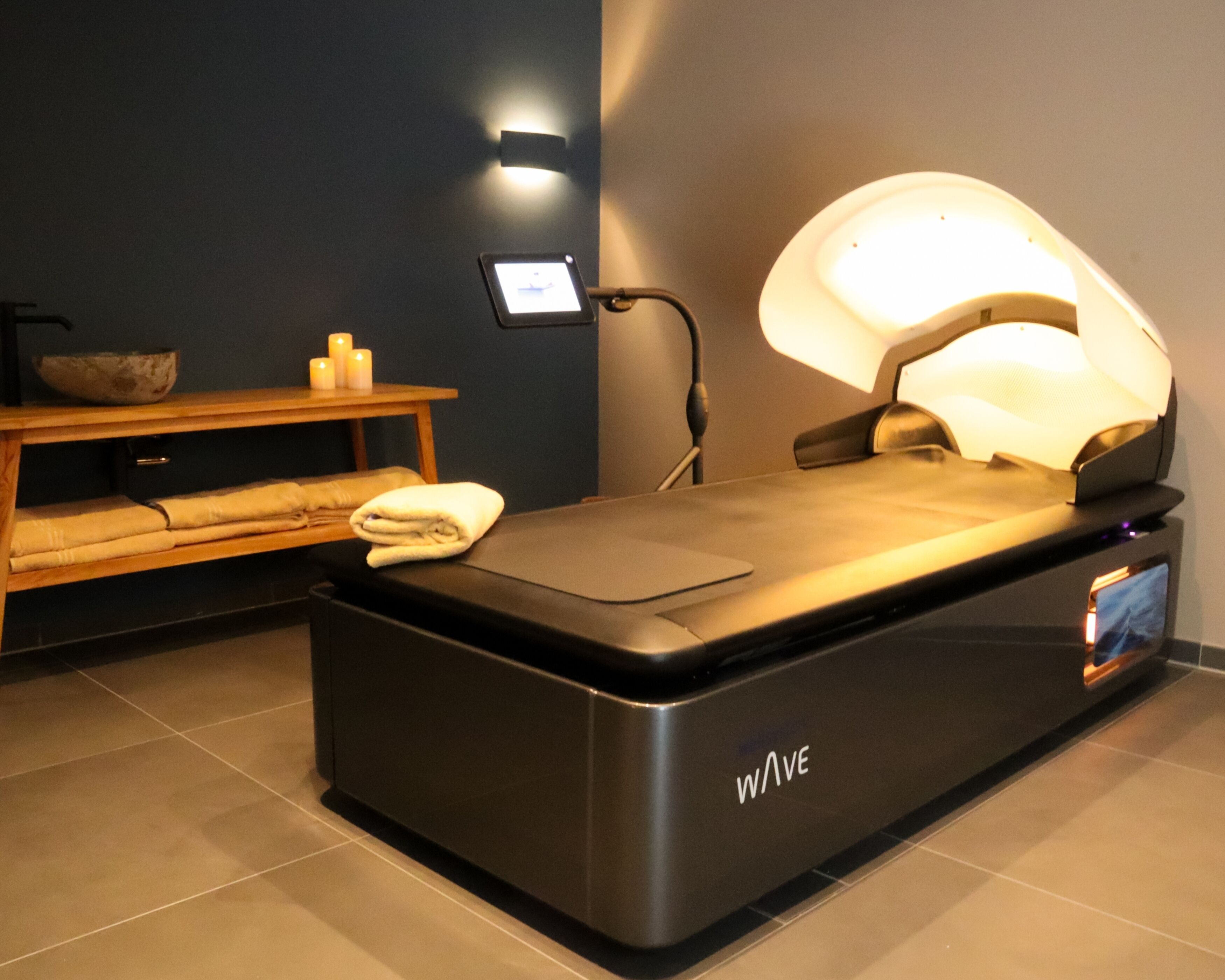 Sala de massagem com mesa preta, iluminação fixada na parede e uma tela pequena exibindo um vídeo.