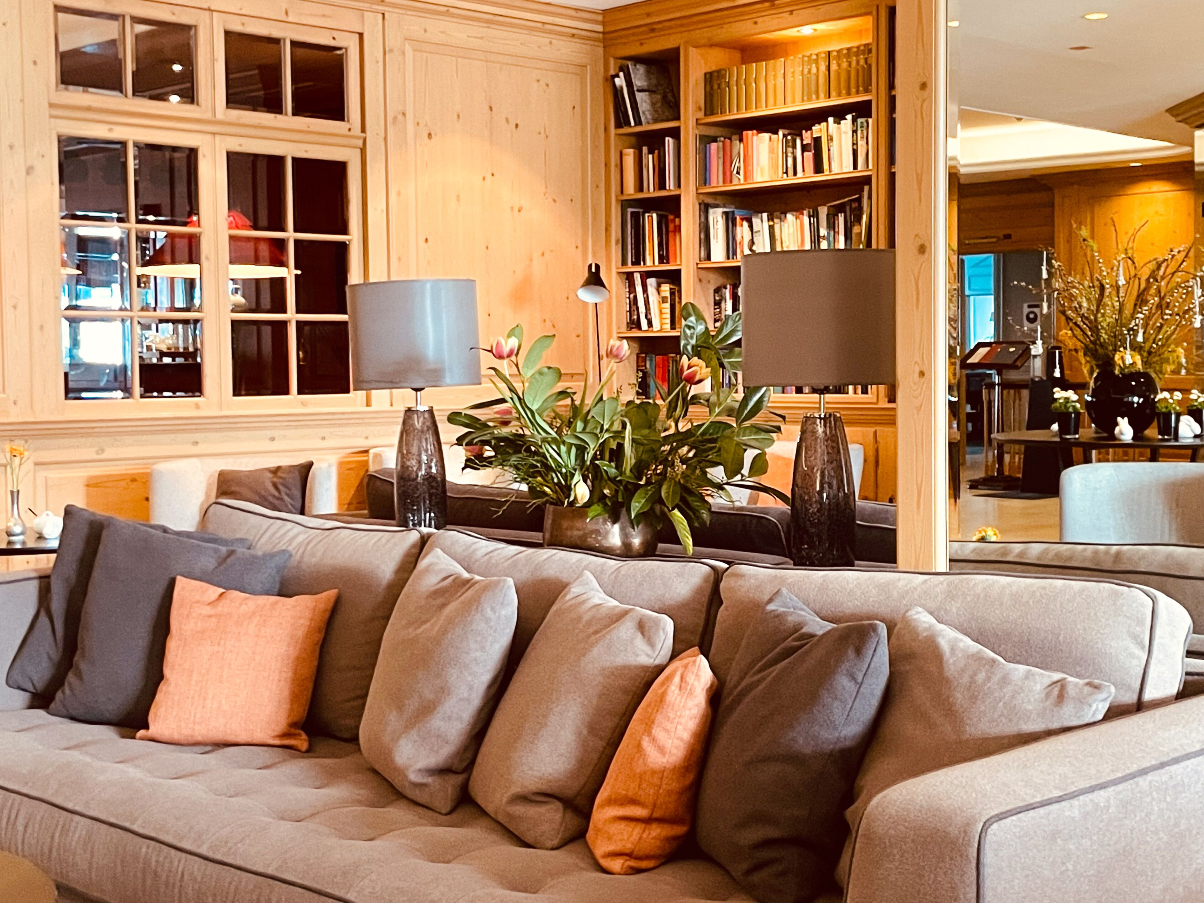 A living room with a beige sectional sofa, a bookshelf, and a potted plant.