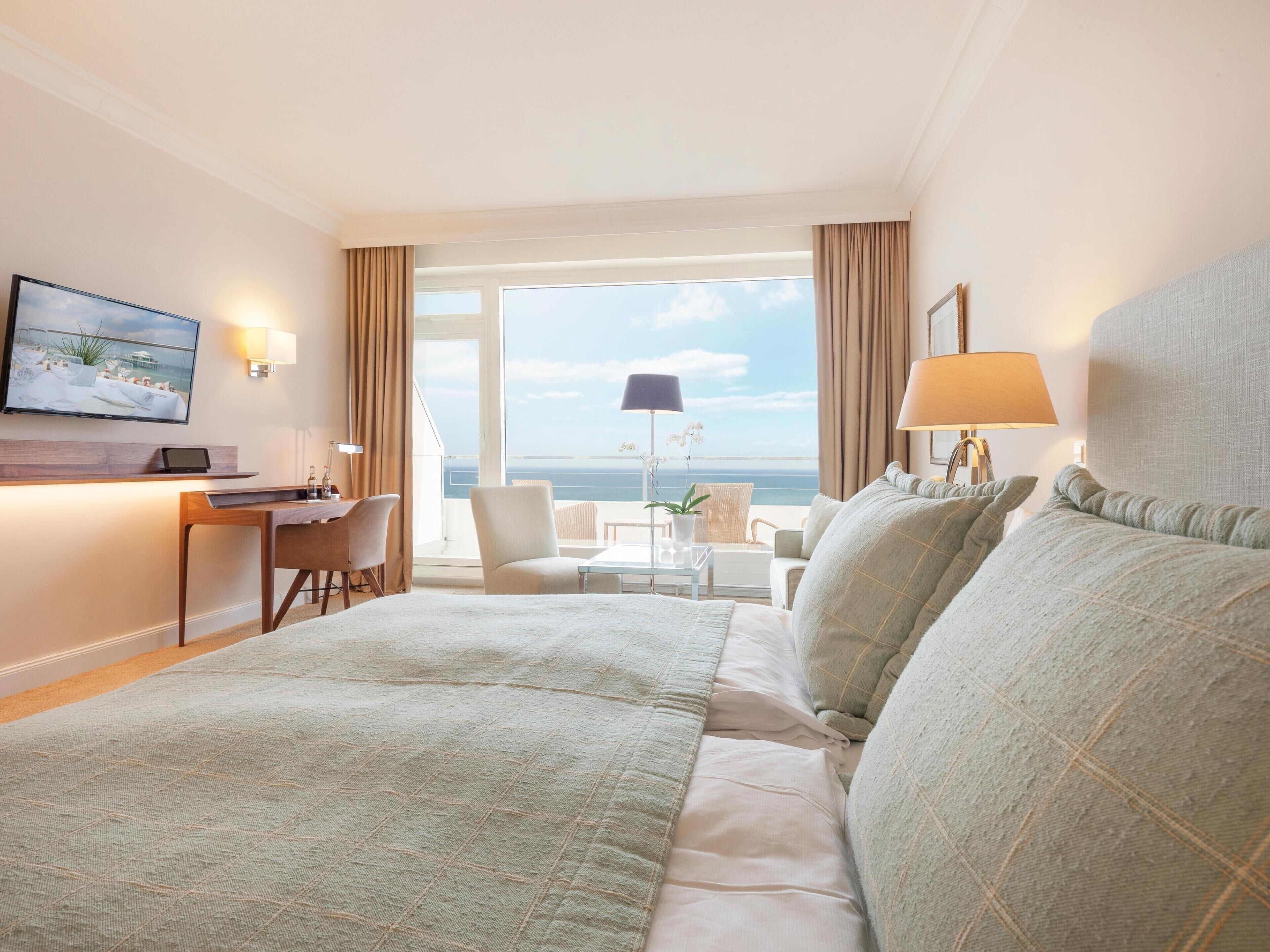 A hotel room with a large bed, a desk, a chair, and a view of the sea.