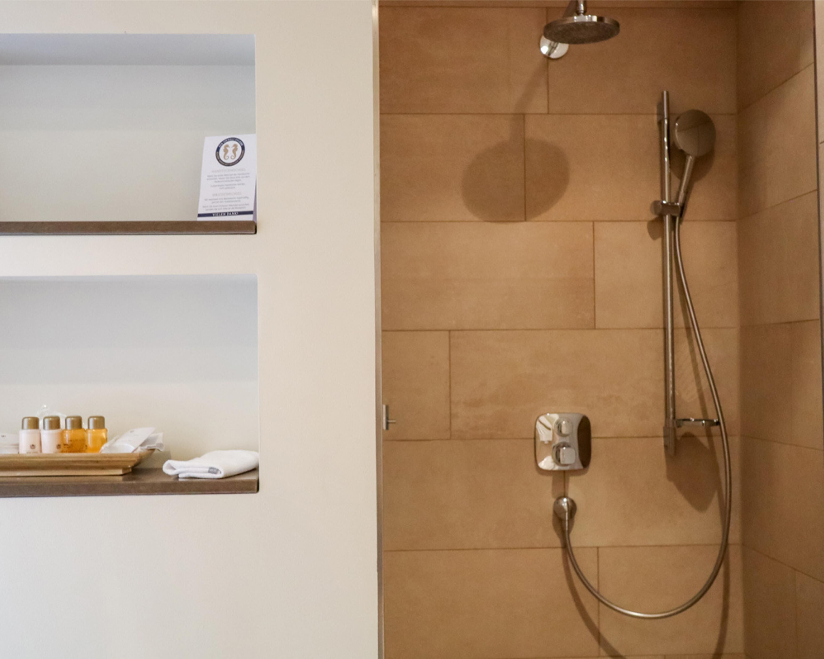 A shower with a handheld showerhead and a wall-mounted faucet, a towel rack, and a shelf with toiletries.