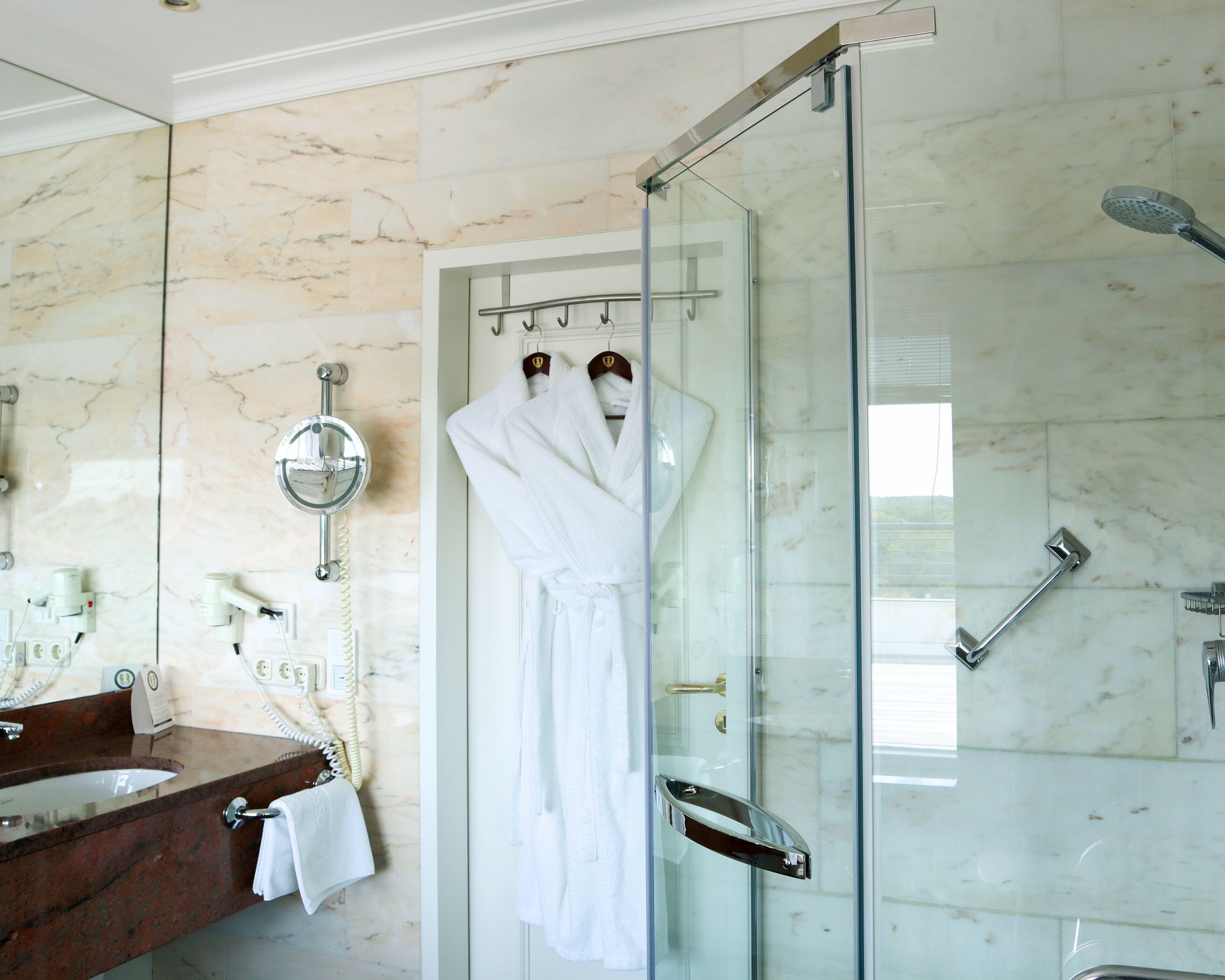 Une salle de bain avec une douche à parois de verre, un mur recouvert de carreaux de marbre, un lavabo avec un miroir et un porte-serviettes.