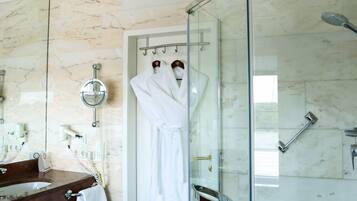 Une salle de bain avec une douche à parois de verre, un mur recouvert de carreaux de marbre, un lavabo avec un miroir et un porte-serviettes.