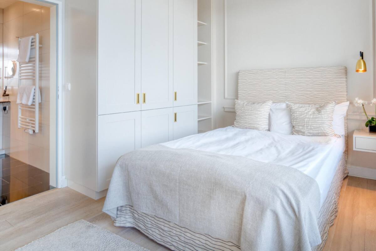 A modern bedroom with a large bed, white wardrobe, and a bedside table with a lamp.