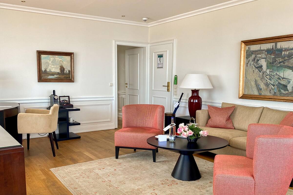 A living room with a beige sofa, two armchairs, a coffee table with flowers, a lamp, and a painting on the wall.