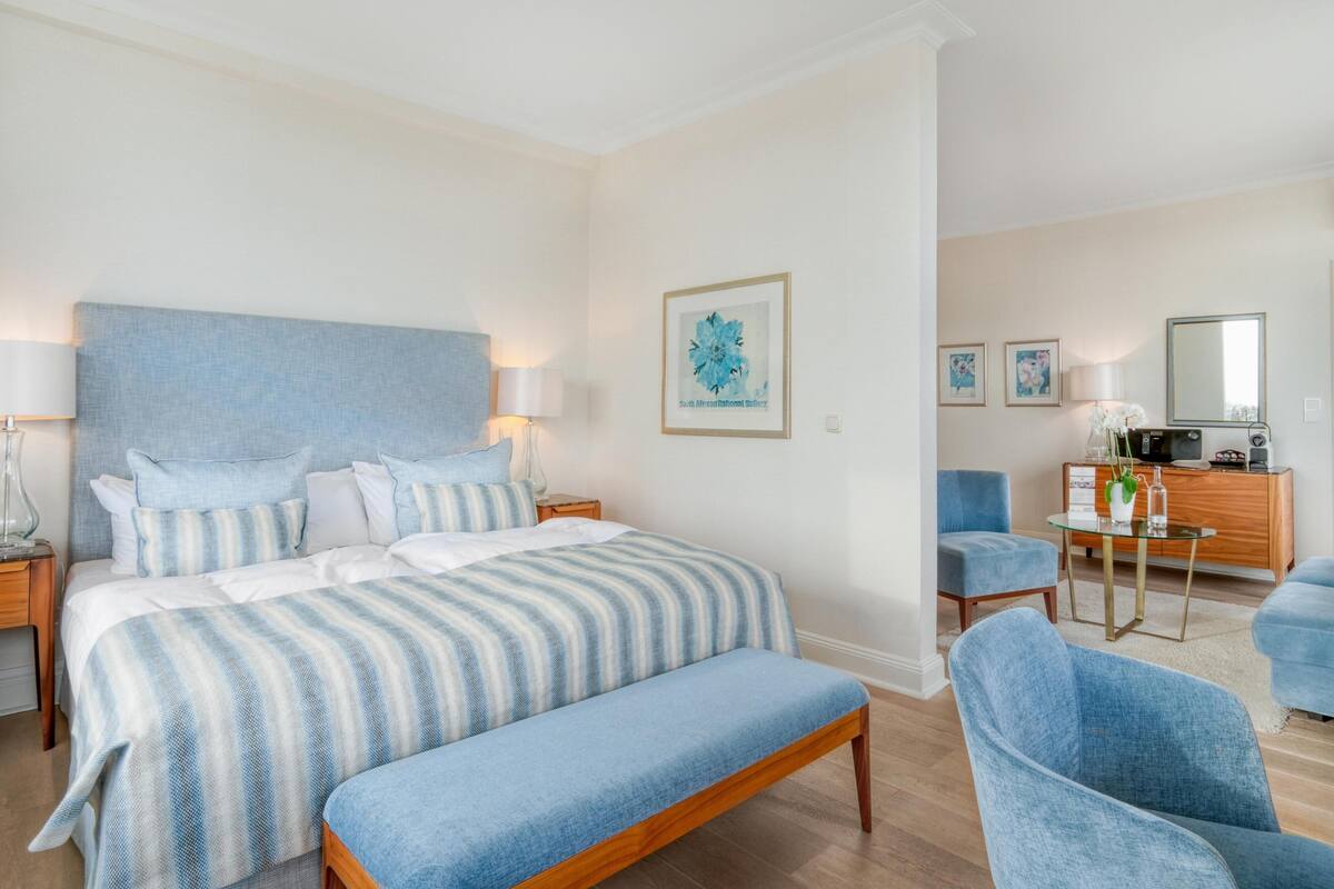 A bedroom with a large bed, a bedside table, a chair, a dresser, and a mirror.