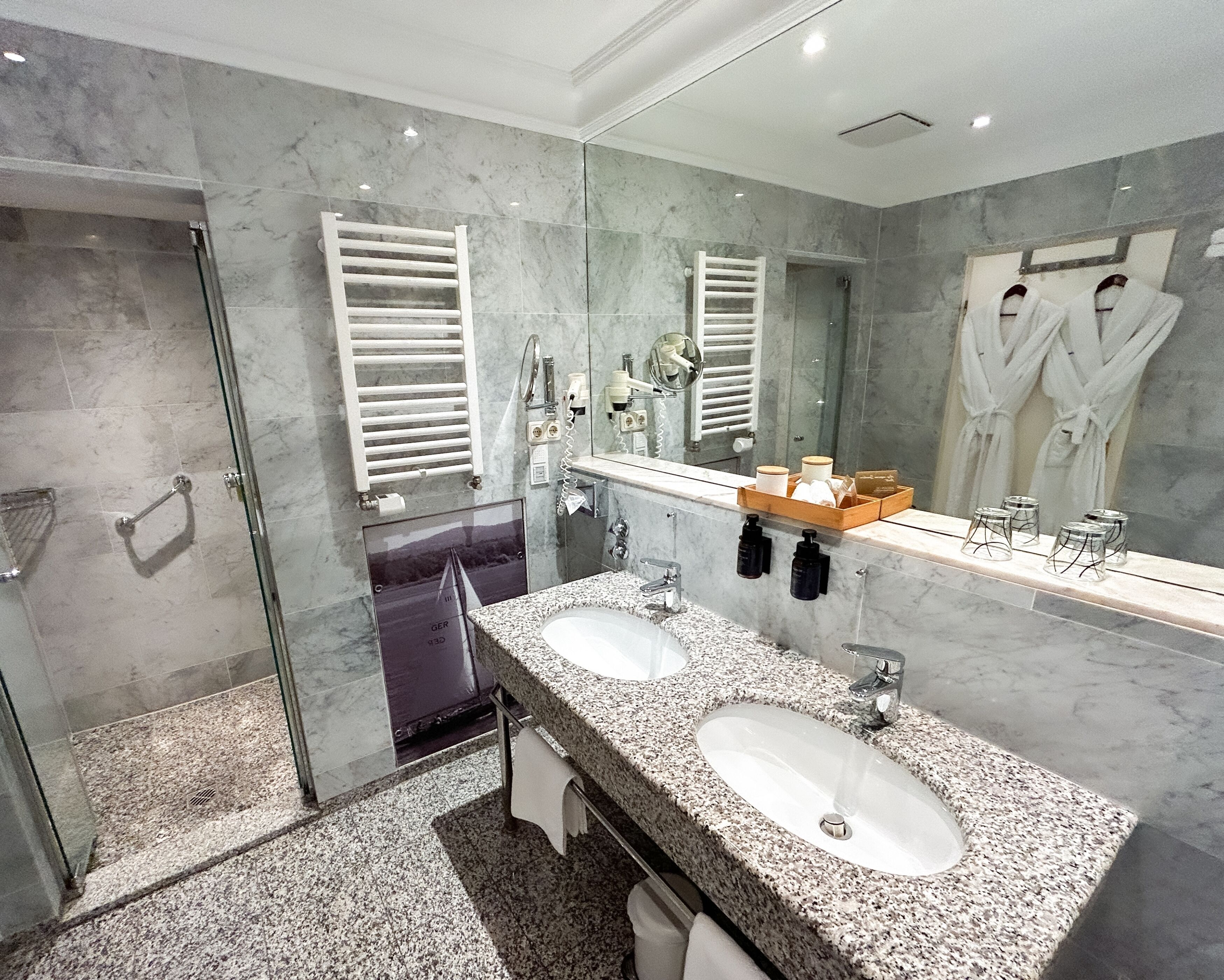 A modern bathroom with two sinks, a glass shower enclosure, and a large mirror.