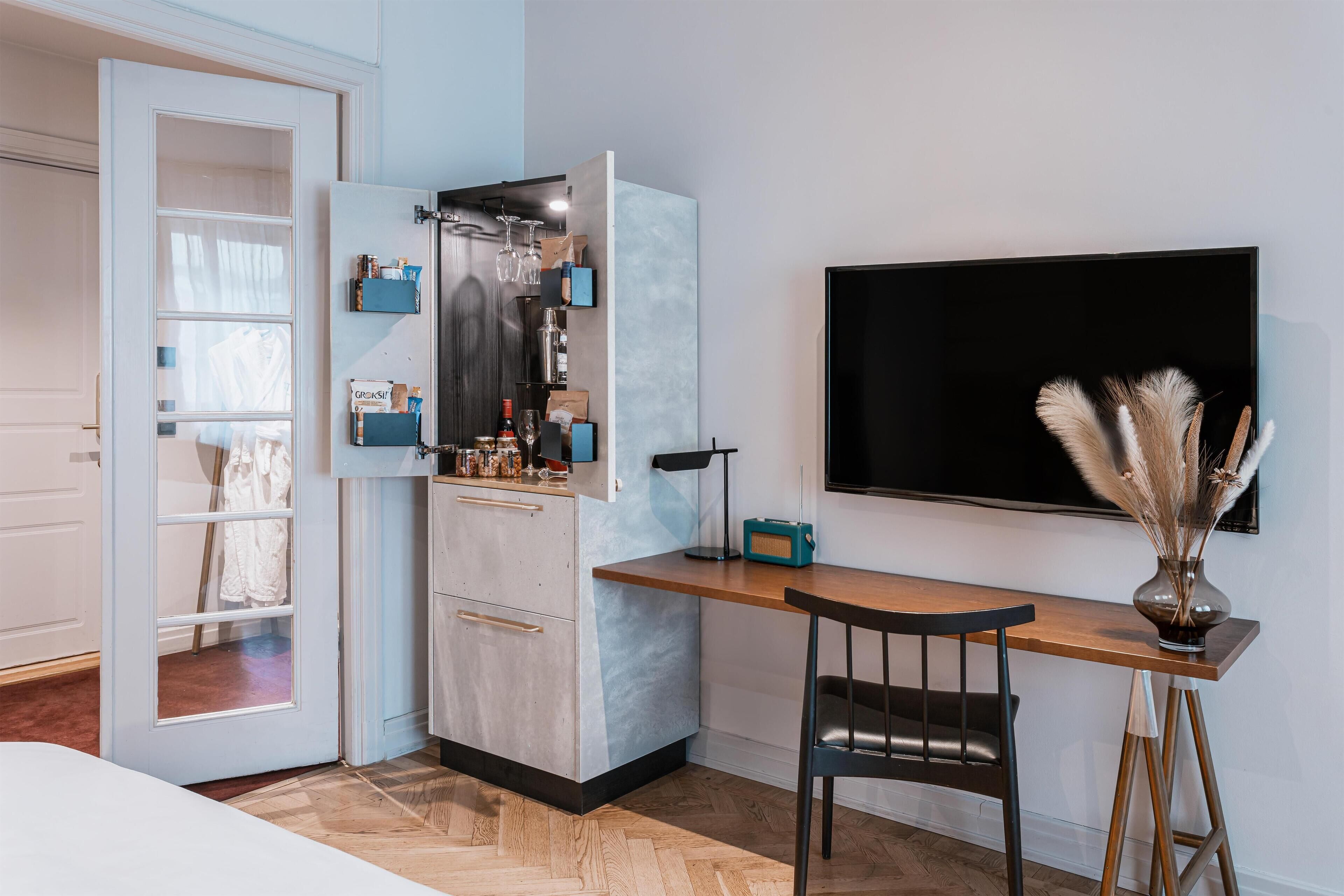 A compact kitchen with a built-in fridge, a wooden dining table, and a TV mounted on the wall.