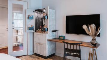 A compact kitchen with a built-in fridge, a wooden dining table, and a TV mounted on the wall.