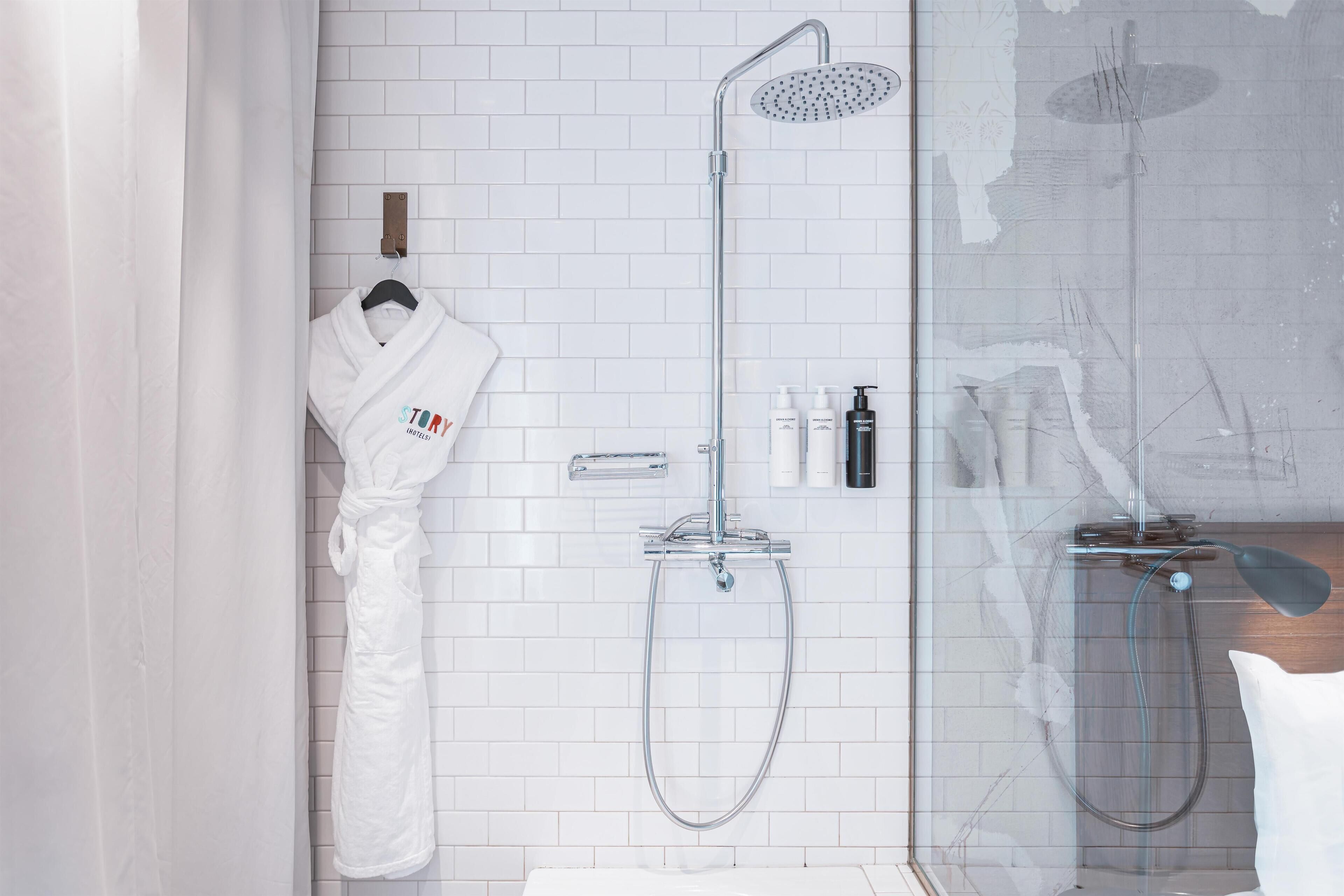 A modern bathroom with a glass shower enclosure, a white robe hanging on the wall, and toiletries on a shelf.