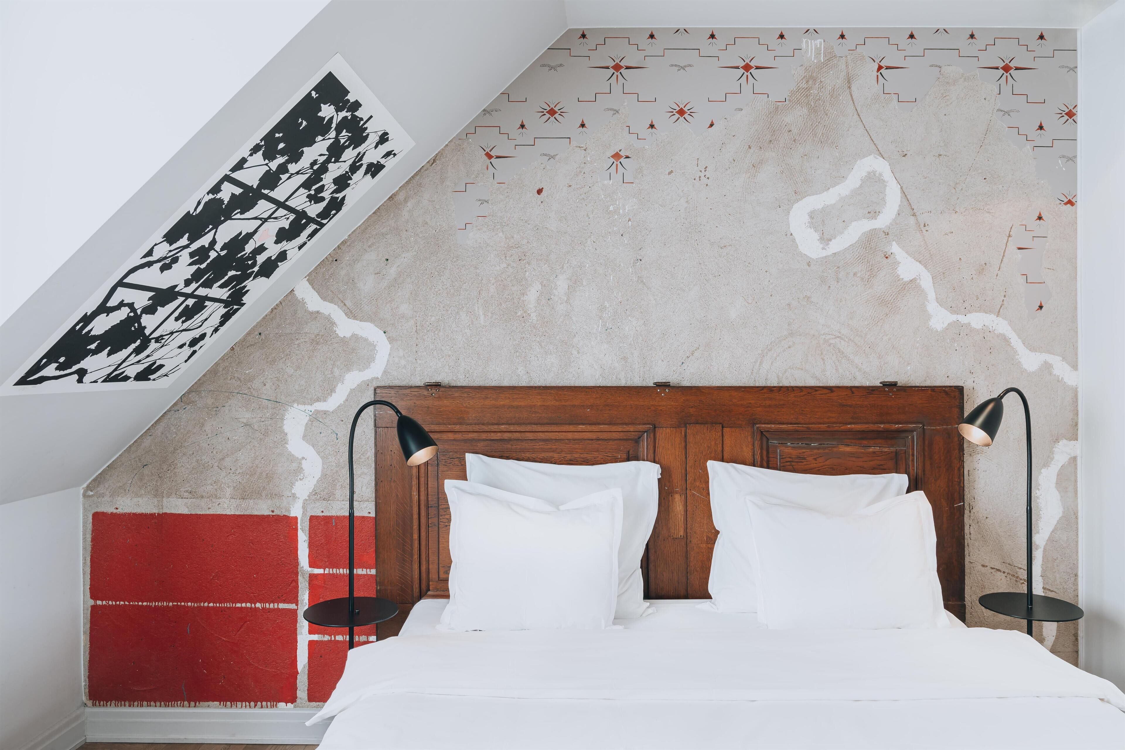 Een slaapkamer met een houten hoofdbord, wit beddengoed en een rode accentmuur.