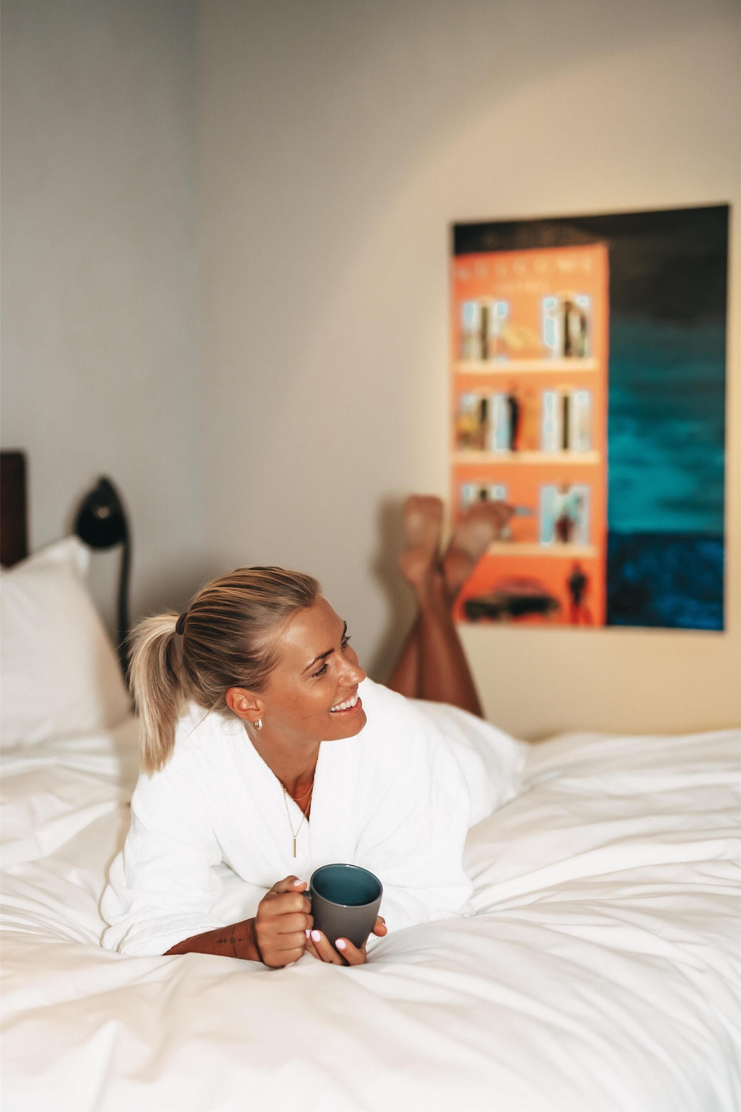 A person lying on a bed in a room with a bookshelf and a painting on the wall.