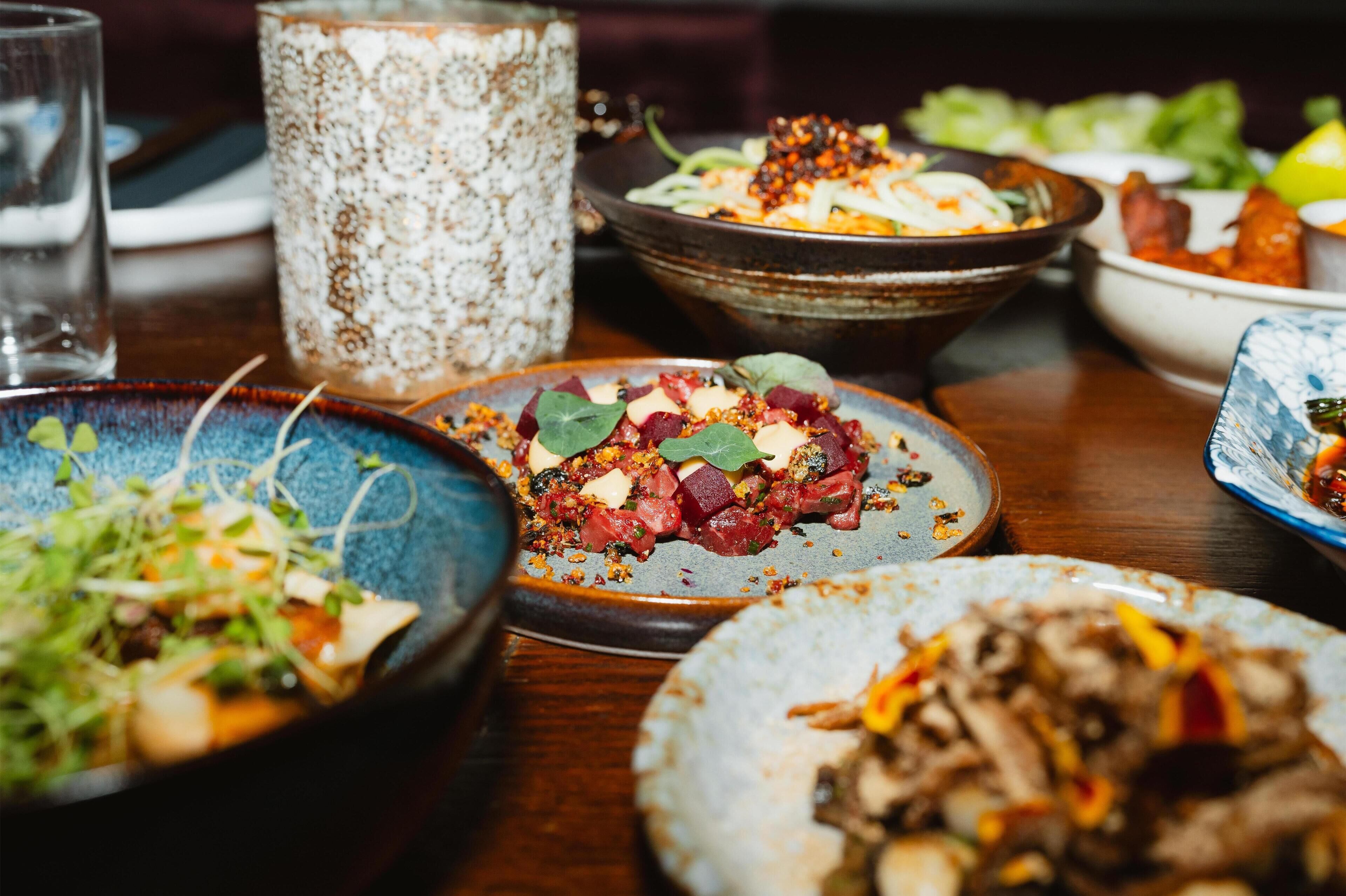 A dining table with various dishes, including a bowl of salad, a bowl of meat, and a bowl of soup.