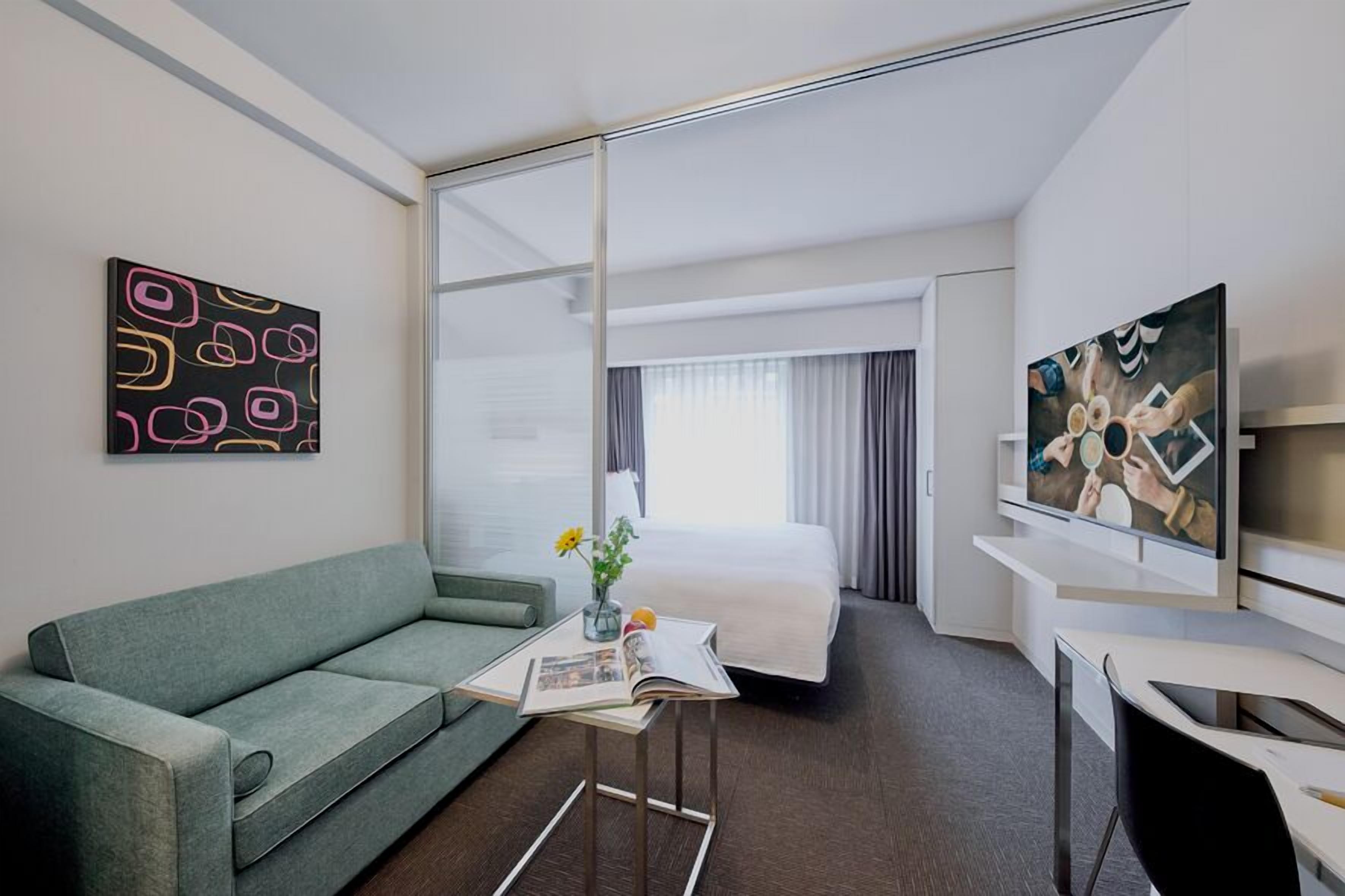 A hotel room with a bed, a sofa, a TV, a coffee table, and artwork on the walls.