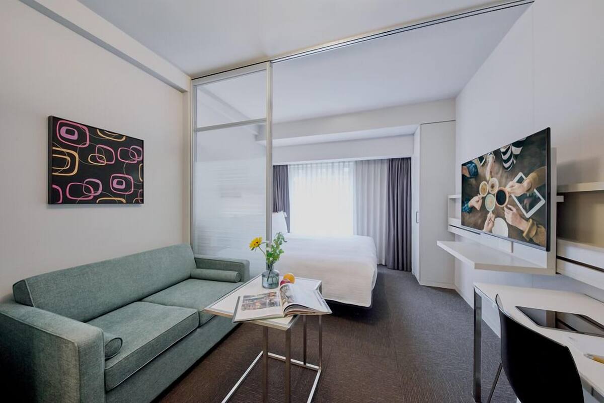 Ein Hotelzimmer mit einem Bett, einer Couch, einem Fernseher, einem Couchtisch und Kunstwerken an den Wänden.